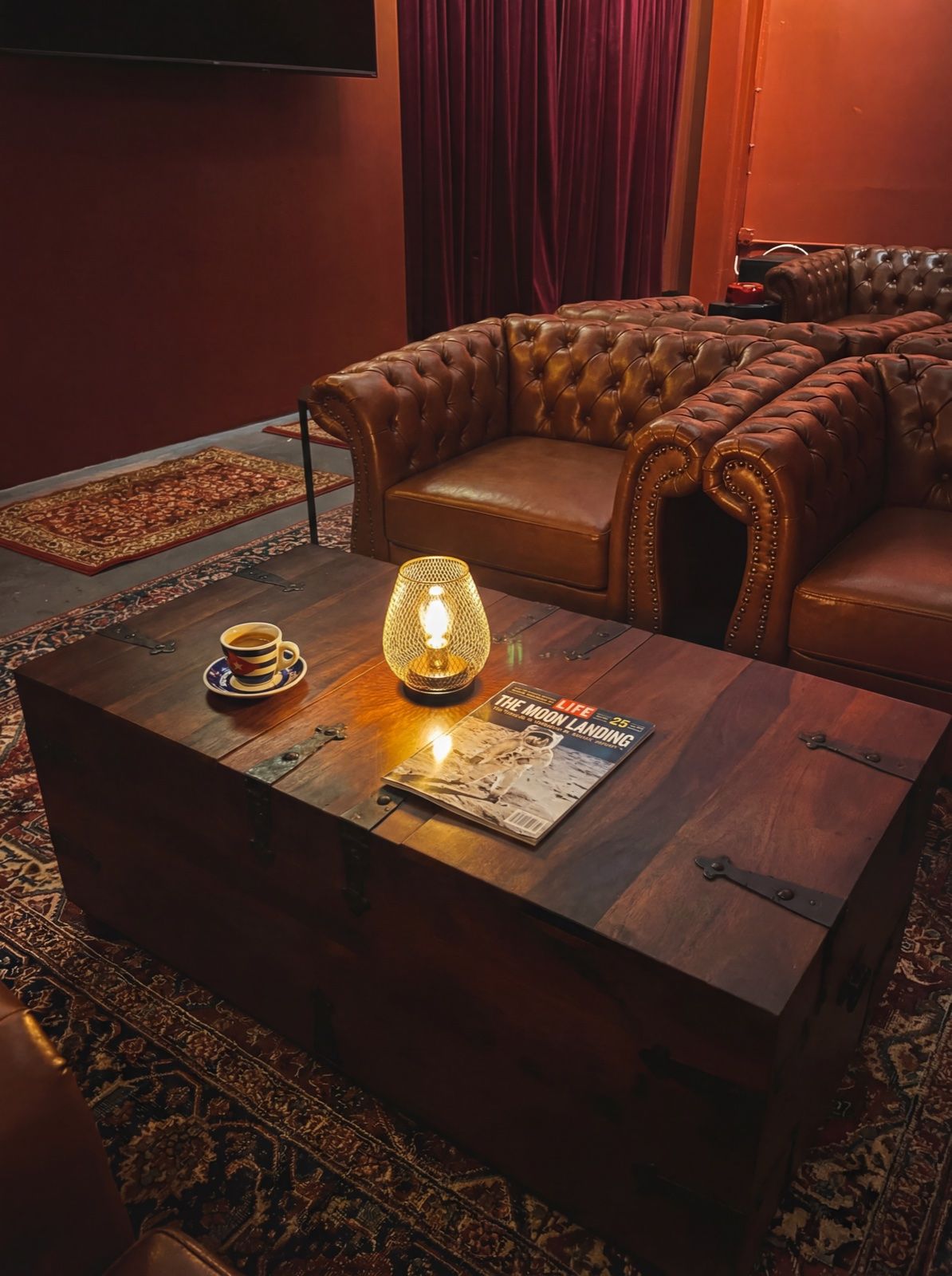 Atmospheric interior with vintage trunk coffee table, Edison lamp, LIFE magazine, and velvet curtains